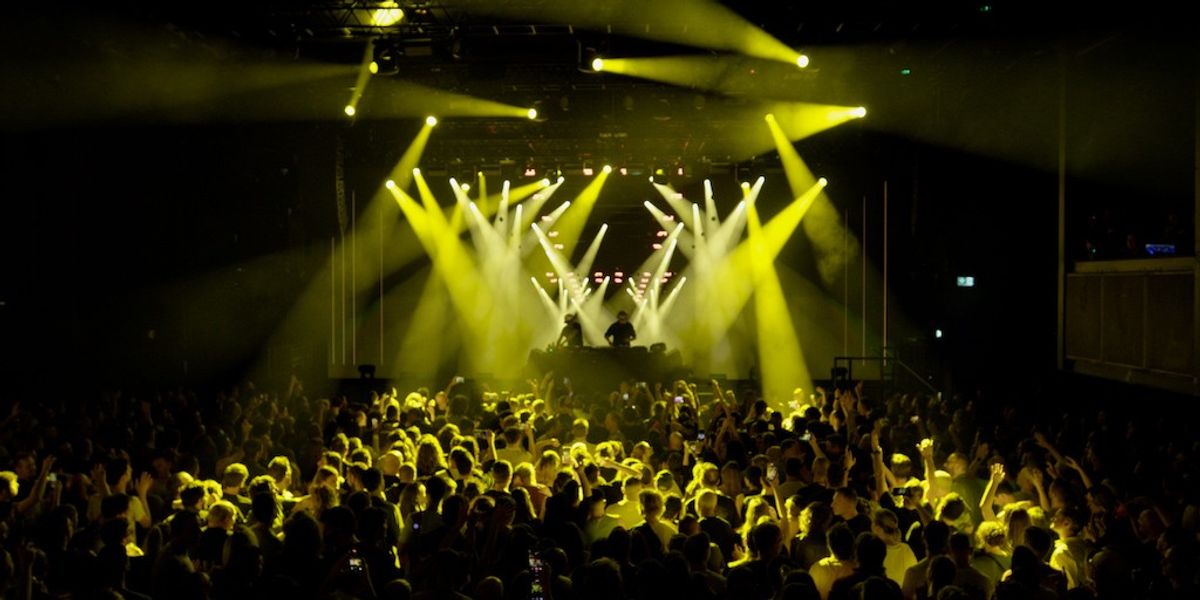 crowd at a royksopp concert with a dj and yellow stage lights powered by dimension real time tech fkeLV6